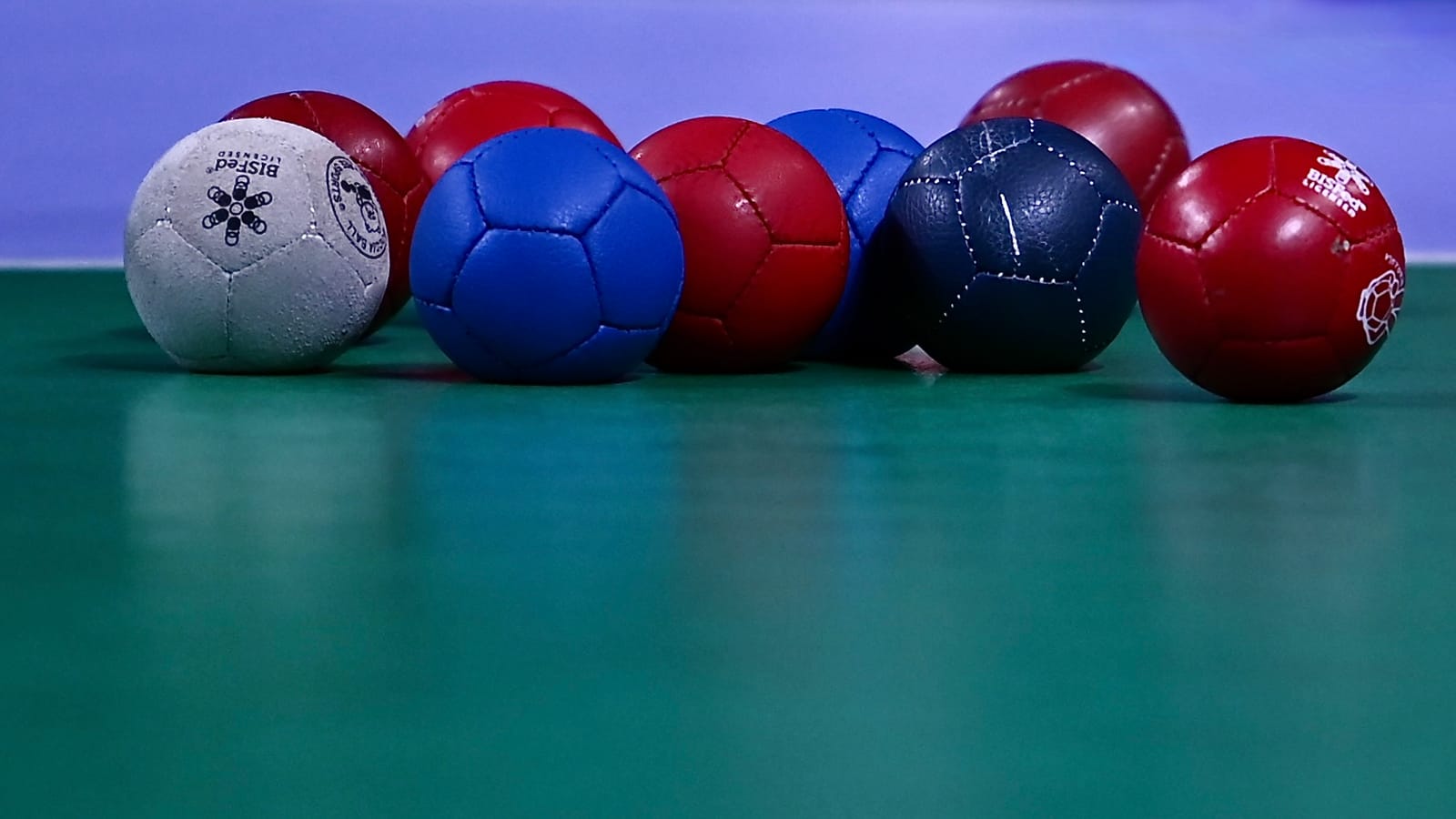 A match set of red and blue leather boccia balls resting beside the white jack on a green court